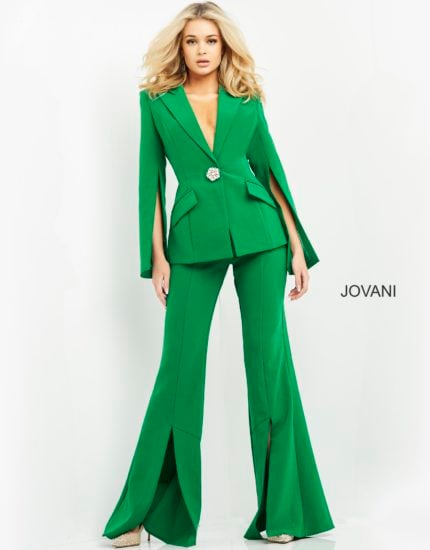 Model wearing Jovani 06922 emerald green jumpsuit with cape sleeves and brooch detail, front view.