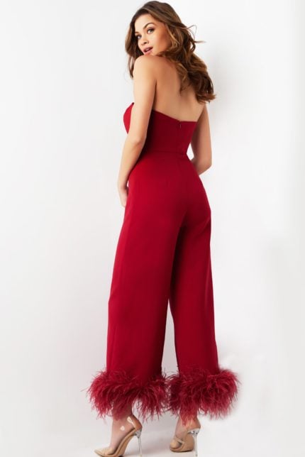 Model wearing Jovani 22590 red strapless jumpsuit with feathered hems, back view.