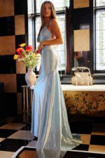 Model in Jovani 23010, displaying back design of blue gown.