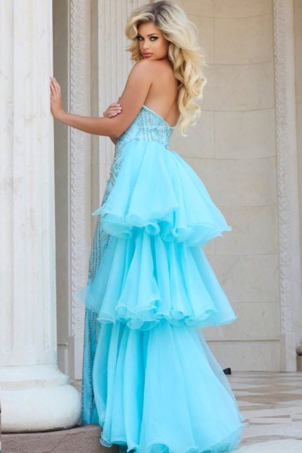 Model wearing Jovani 24565 blue gown with cascading ruffles, back view.