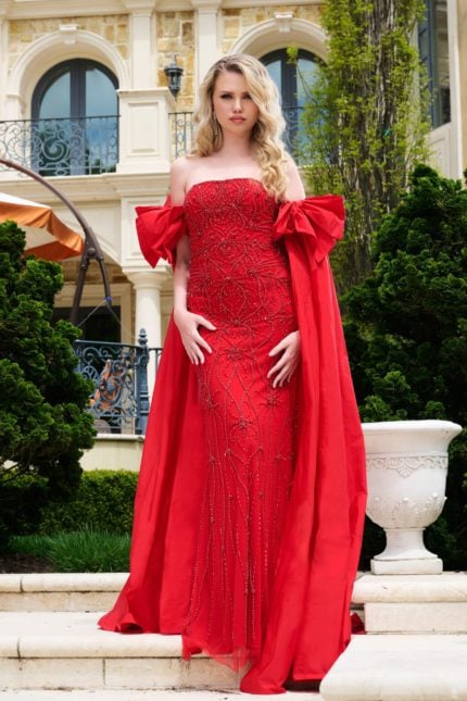 Model wearing Jovani 39377, red gown with intricate beadwork and dramatic bows, front view.