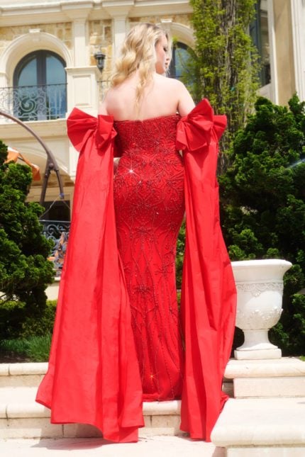 Model wearing Jovani 39377, red gown with intricate beadwork and dramatic bows, back view.