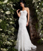 Model wearing JB02836 elegant white gown with lace appliqués, front view, surrounded by flowers