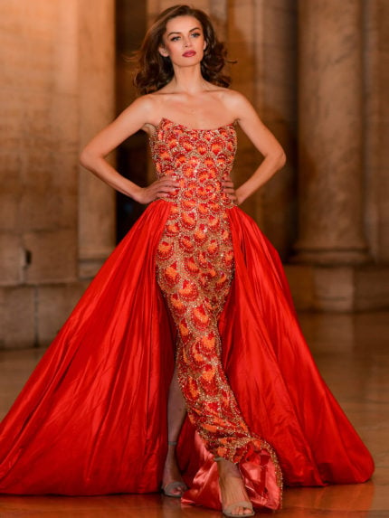 Model displaying the S04603 orange gown with elegant beadwork and a dramatic overlay.