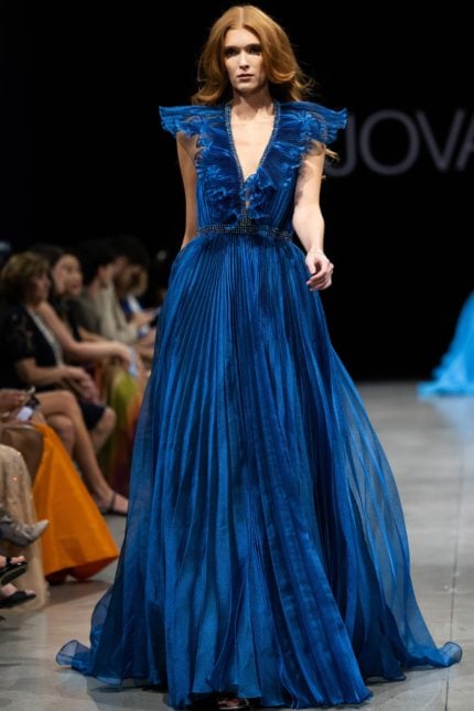 Model wearing Jovani S22362 elegant blue dress with deep V-neckline, ruffled details, and flowing A-line silhouette.