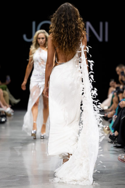 Model wearing Jovani S23231 white gown with feathered back detail, back view.