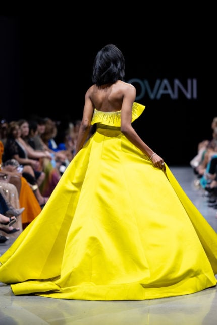 Back view of model wearing Jovani S36369 yellow gown with voluminous skirt