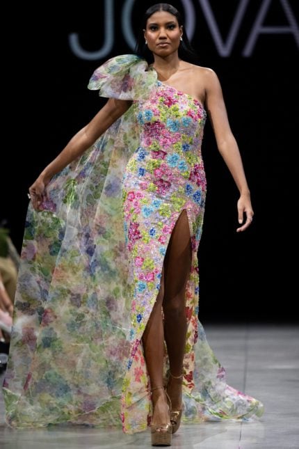 Model wearing Jovani S37492 multi-color floral gown seen from the back with a dramatic cape detail.