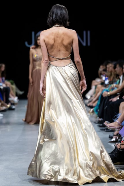 Back view of model wearing Jovani S37498 gold gown with delicate strapping.