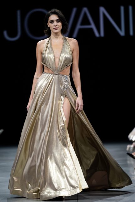 Model wearing Jovani S37498 gold gown with halter neckline and high slit.