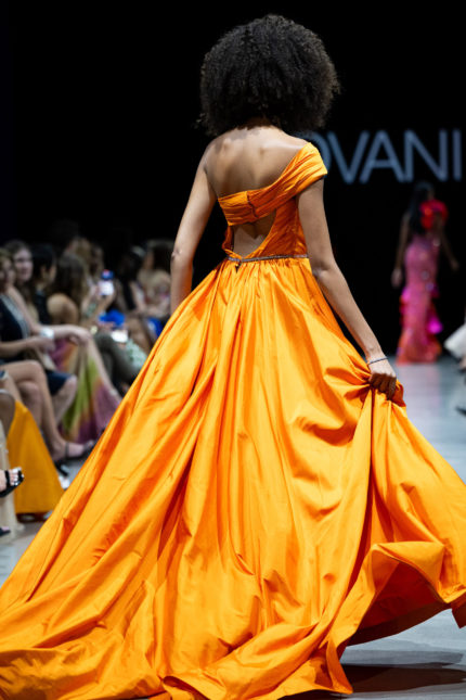 Back view of model wearing S38441 orange gown with flowing skirt