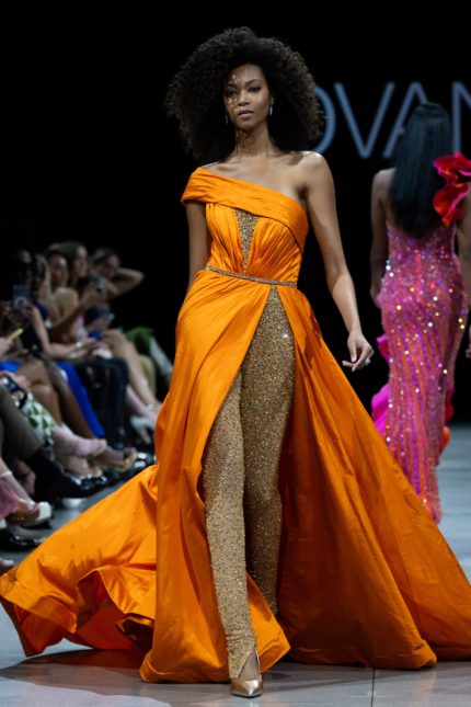 Model wearing S38441 orange gown with off-the-shoulder neckline and high slit