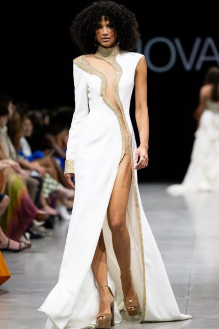 Model wearing Jovani S38446 white gown featuring a high neckline, embellishments, high slit, and full-length sleek design.