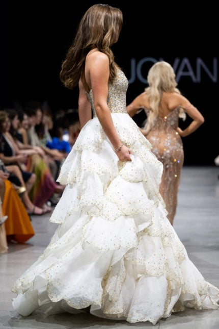 Model wearing Jovani S38886 white gown with layered skirt, side view