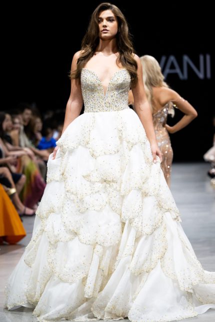 Model wearing Jovani S38886 white gown with deep V-neck and layered skirt, front view