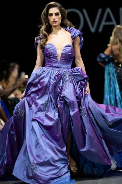 Model wearing Jovani S39133 purple gown with deep V-neck and voluminous skirt